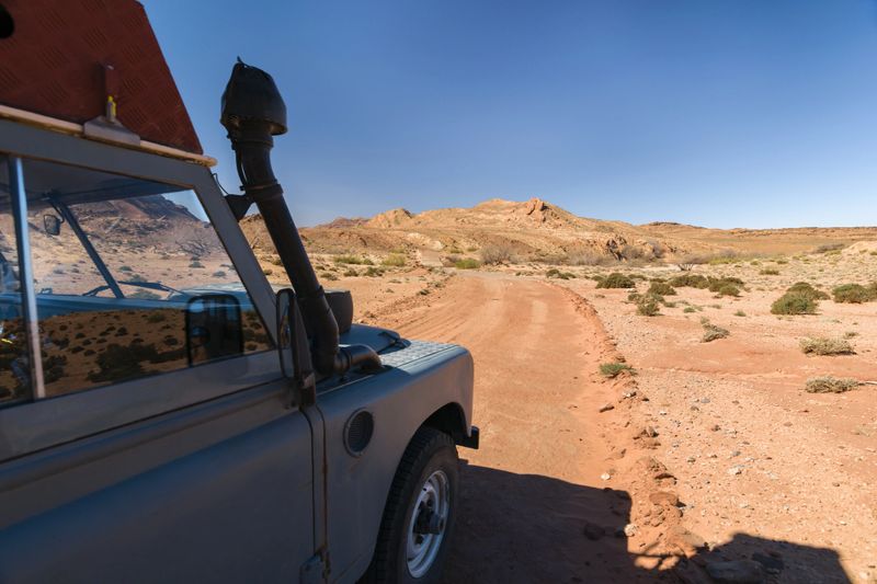 Side of an four by four oldtimer off-road vehicle driving off- road in a desert in Morocco. The vehicle is fully equipped with roof rack  and other off- road items.