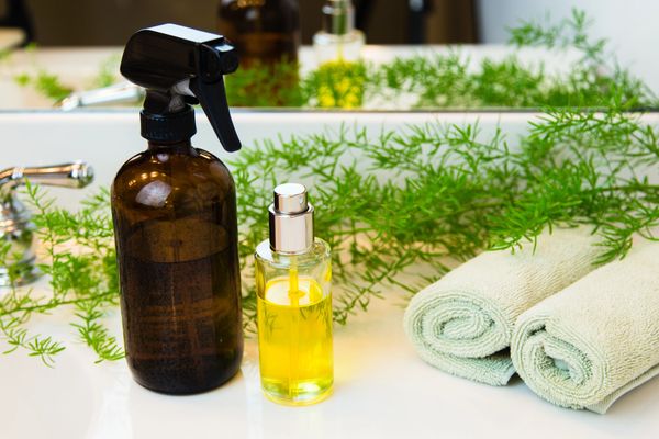 Two spray bottles and rolled towels on a bathroom counter with greenery.