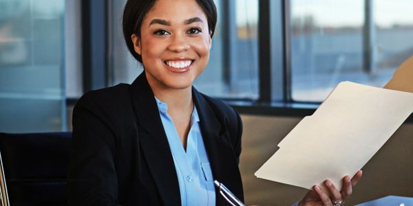 Smiling professional woman holding documents and pen at office desk.