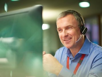 Smiling customer service representative wearing a headset at his computer.