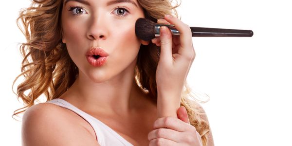 Young woman applying makeup with a brush, making a surprised expression.