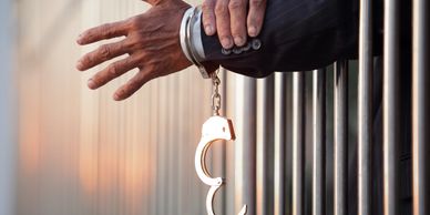 A handcuffed hand reaching out from behind prison bars.