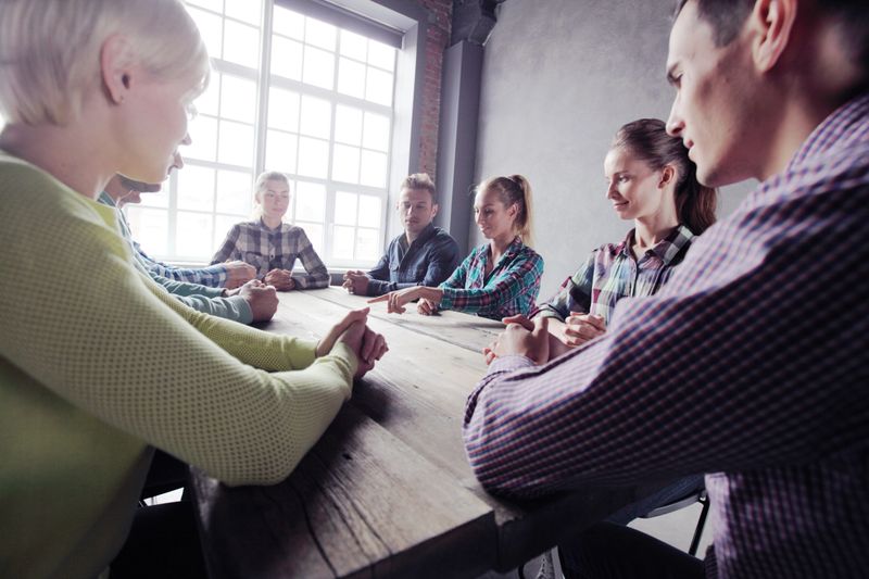 Team of people in casual clother working together sitting around wooden table and pointing at center, startup concept