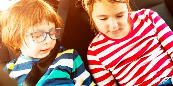 Two children in striped shirts sitting in a car, focused on something in front of them.