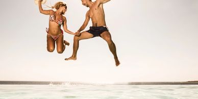 Couple joyfully jumping into a pool on a sunny day, holding hands and smiling.