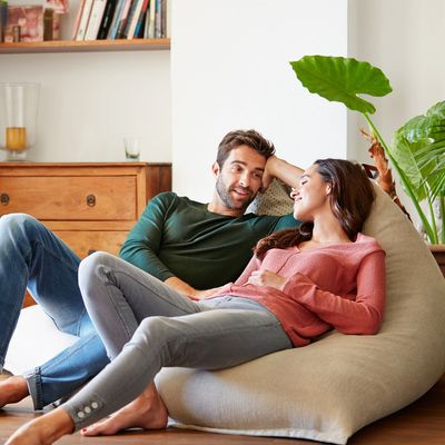 Couple relaxing and smiling on a beige bean bag in a cozy living room.