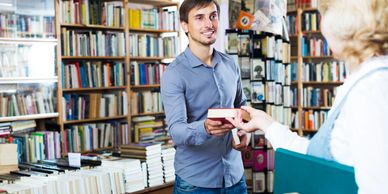 Man helping woman with book purchase.