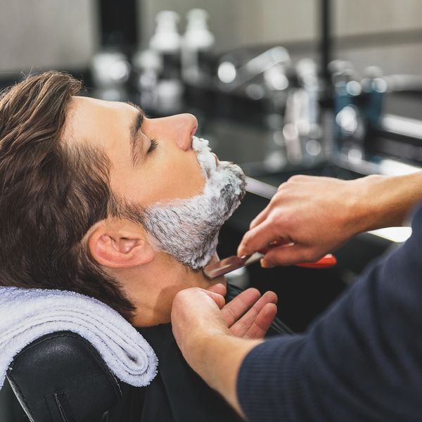 Man getting a professional straight razor shave at a barbershop.