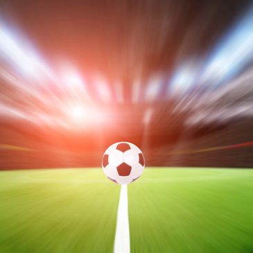 Balón de fútbol al centro de una cancha difuminada.