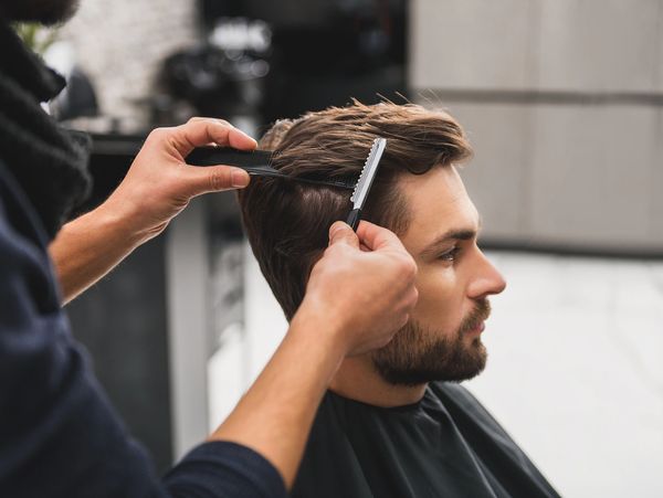 Barber styling a man's hair with a comb and scissors.