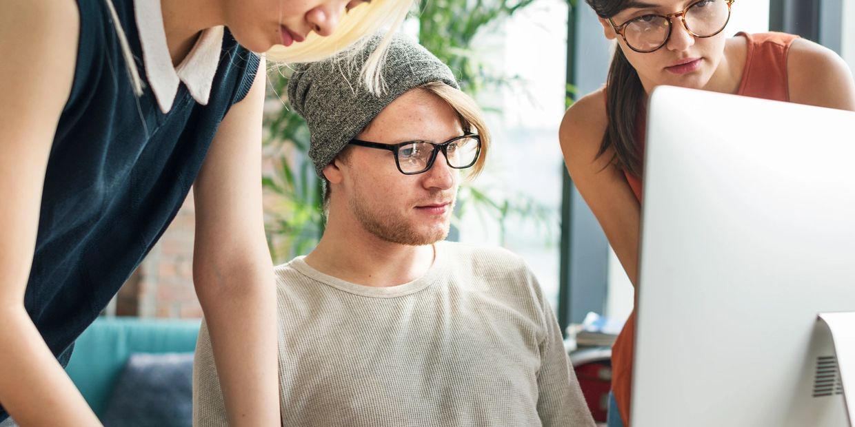 Three young professionals collaborating around a computer in a modern office.