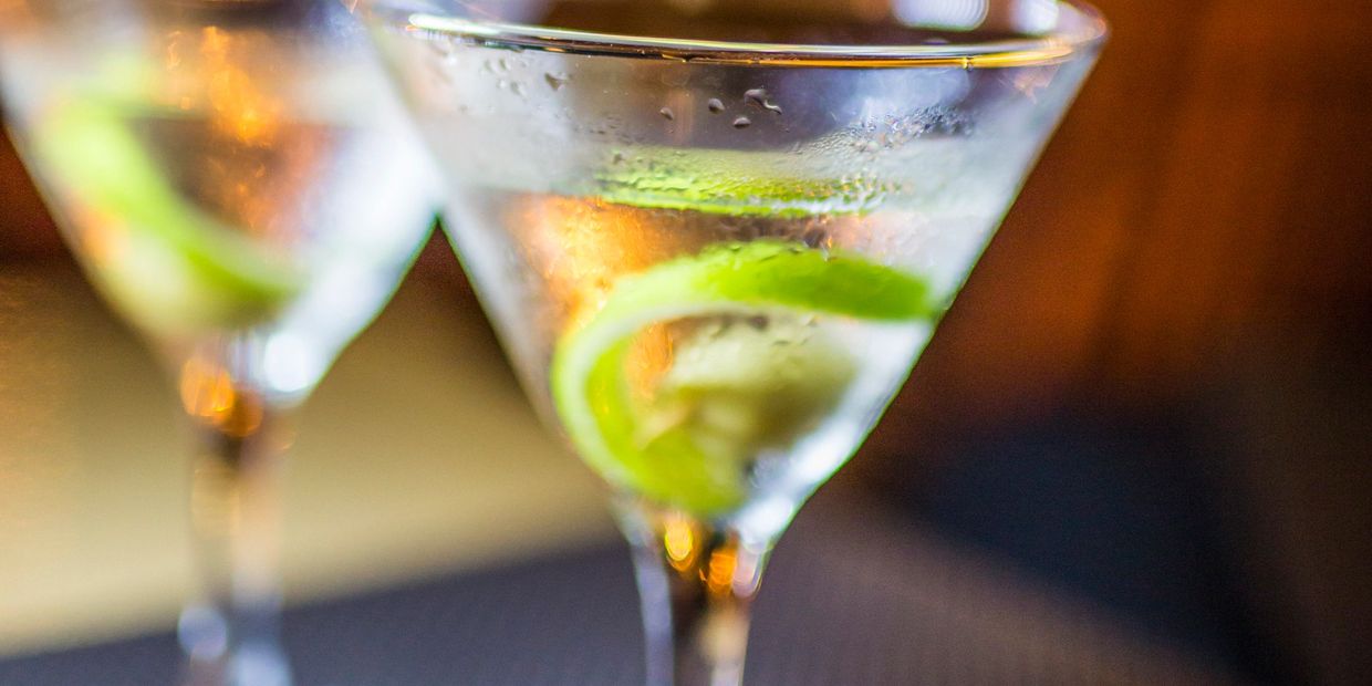 Two martini glasses with lime twists on a dark surface.