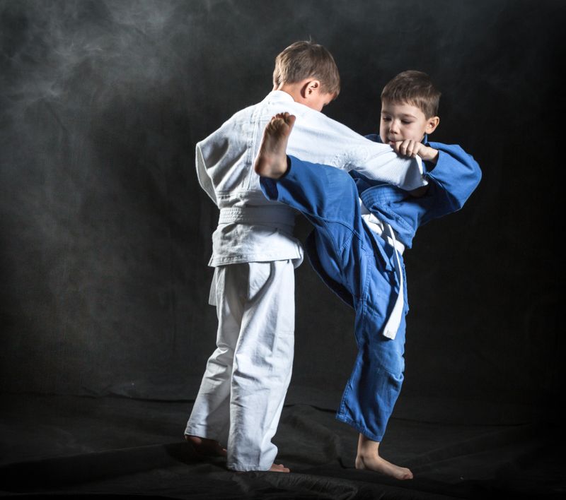 Two elementary aged boys are practicing judo. The boys dressed in sport uniforms judo gi. They are performing training judo fight. Studio shooting in light haze on black background