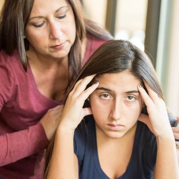 A concerned woman comforts a stressed young girl holding her head.