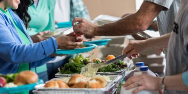 People serving food at a cafeteria line.