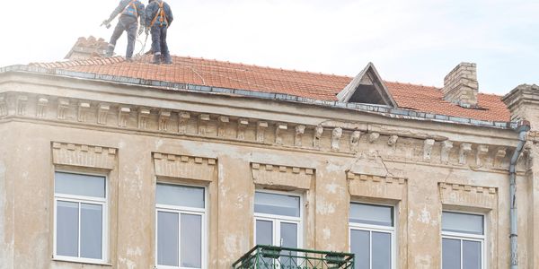 Two workers repairing a rooftop on a historic building.