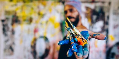 Hand holding paintbrushes covered in blue paint.