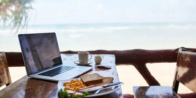 Laptop and breakfast on a wooden table by the beach.