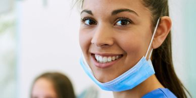Smiling healthcare worker wearing a blue surgical mask below her chin.