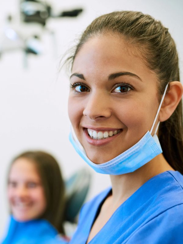Smiling dental professional with patient in background.