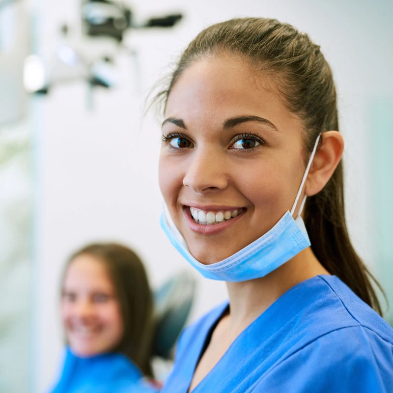 Portrait of a young female dentist standing in her office with a patient in the background