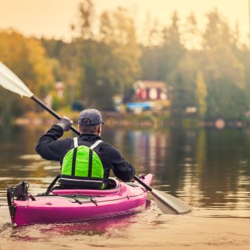 Person kayaking on calm lake at sunset.