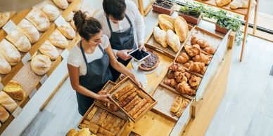 Two bakers arranging fresh bread and pastries in a bakery.