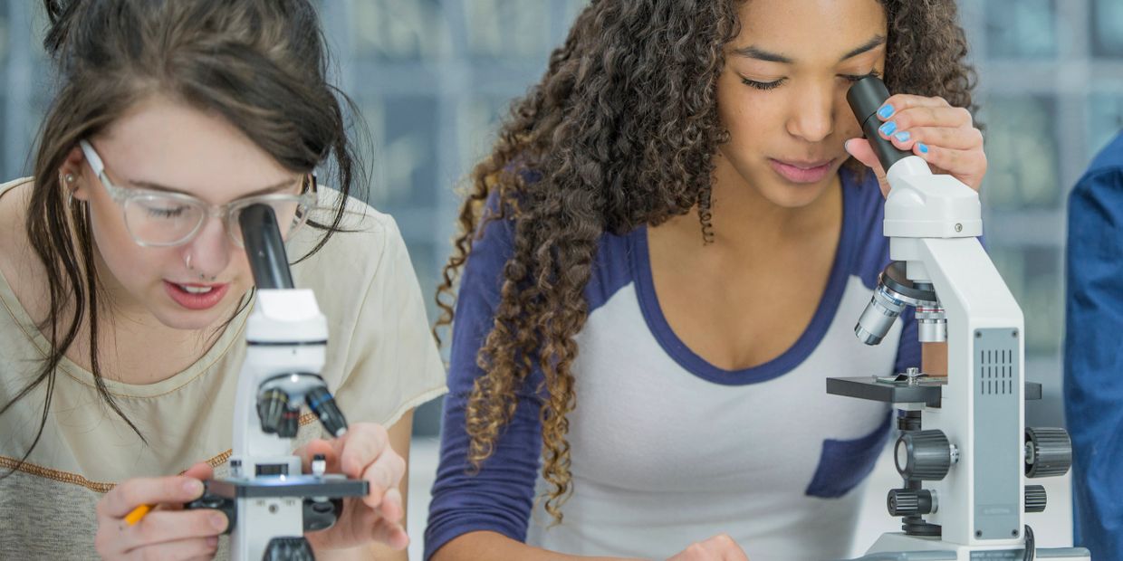 Two young women examining slides using microscopes in a science lab.