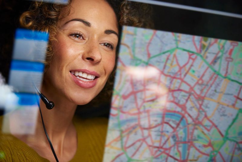a female logistics worker is organising dispatch of freight on her interactive digital map whilst talking on her headset.