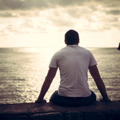 Man sitting on a ledge, looking at the ocean during sunset.