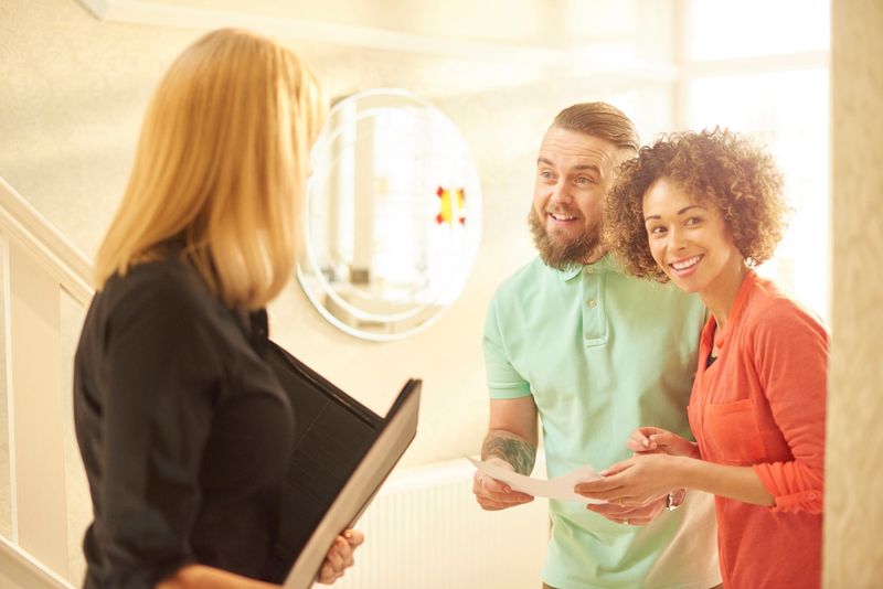 a young couple view a property guided by an estate agent. They are standing in the hallway of house and chatting about the paperwork that they are holding .