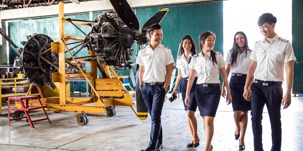 Young aviation students walking in an aircraft hangar, smiling and chatting.