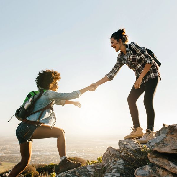 2 women climbing - 1 reaching out to the other to help. Both wearing checked shirts and rucksacks
