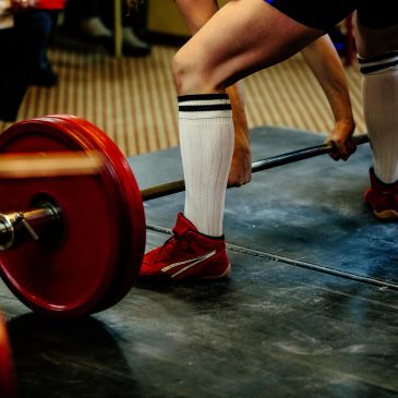 Atleta levantando pesas con calcetas largas y zapatos rojos.