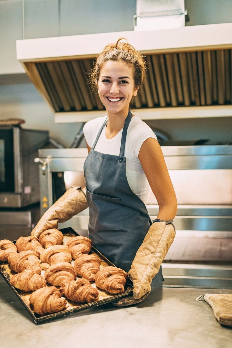 Young baker holding a tray with freshly baked croissants in the bakery