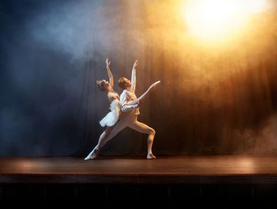 Elegant ballet dancers performing under warm stage lighting.