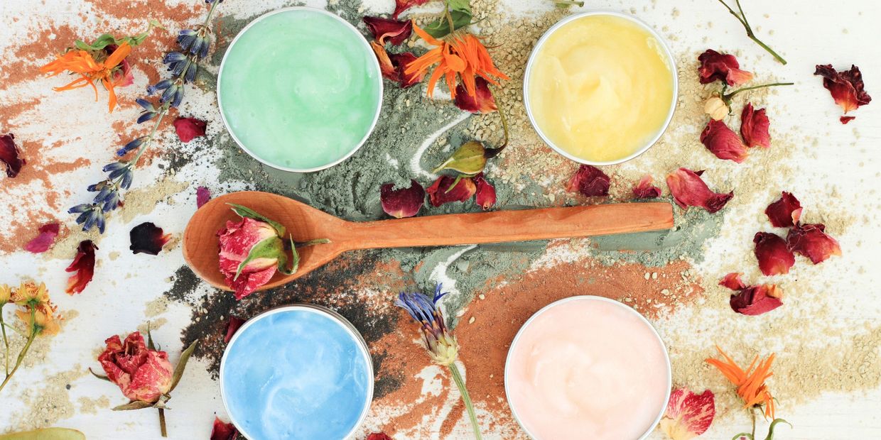 Colorful skincare creams with dried flowers and powders on a white surface.
