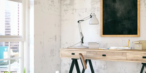 Minimalist workspace with wooden desk, chair, and chalkboard near a window.