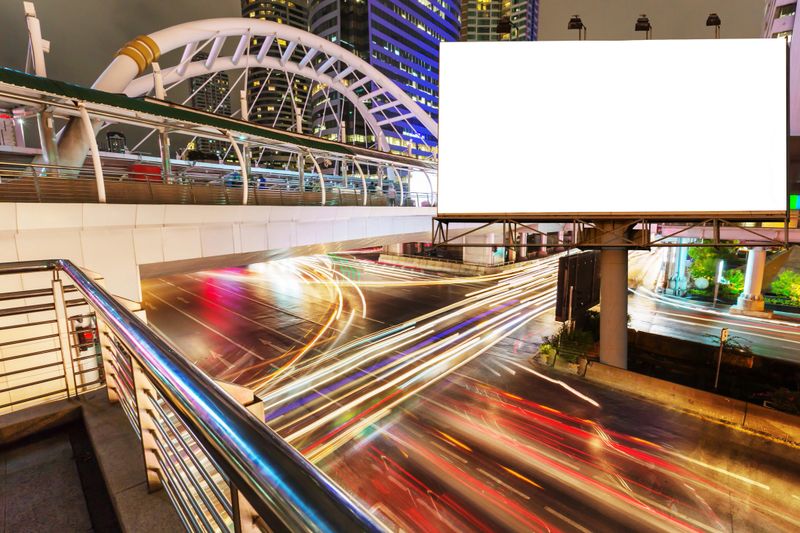 Blank billboard with light trails, street and urban in the night - can advertisement for display or montage product or business.