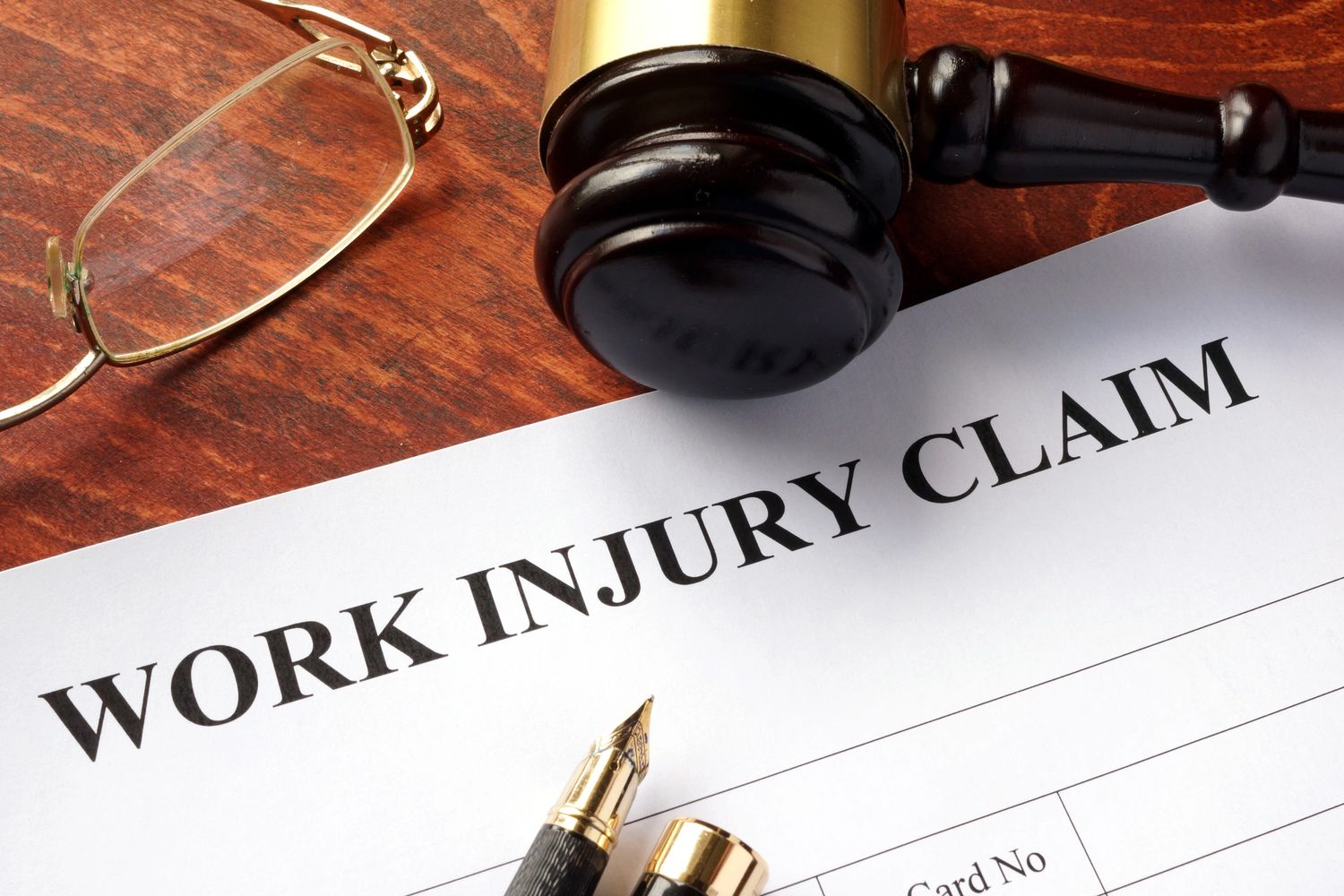 A work injury claim form with a gavel, pen, and glasses on a wooden surface.