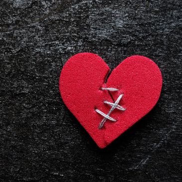 Red heart stitched together on a dark surface.