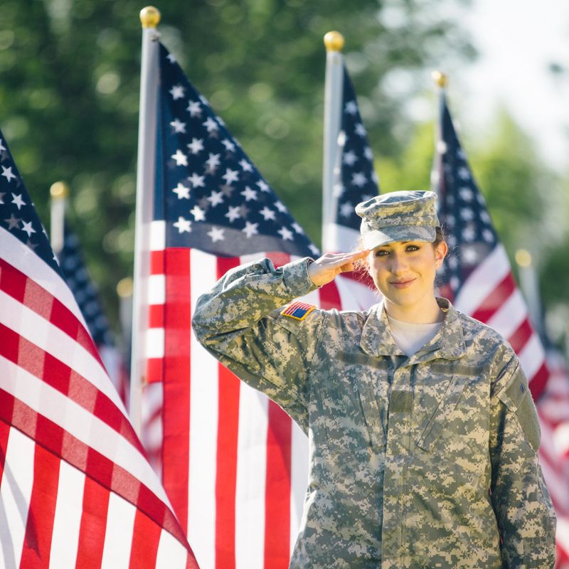 American soldier in uniform saluting while standing in a field of American flags