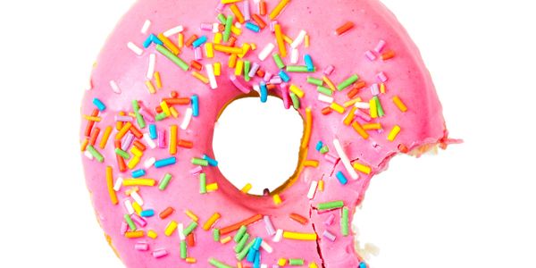 Pink frosted donut with colorful sprinkles and a bite taken out.