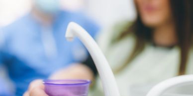 A person holding a purple cup near a dental water dispenser.