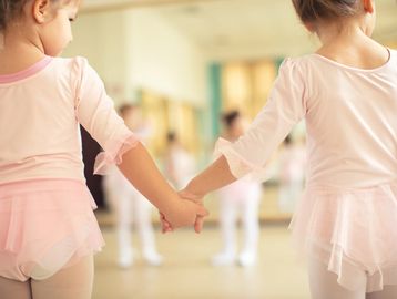 Two young ballerinas holding hands in a dance studio.