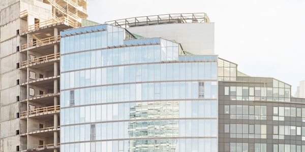 A modern glass building reflecting another skyscraper with an unfinished concrete building beside it.