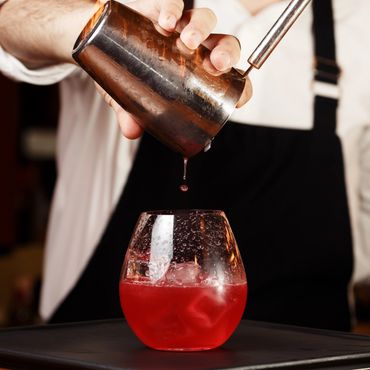 Bartender pouring a red cocktail from a shaker into a glass with ice.