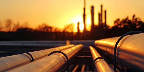 Industrial pipelines at sunset with factory silhouette in background.