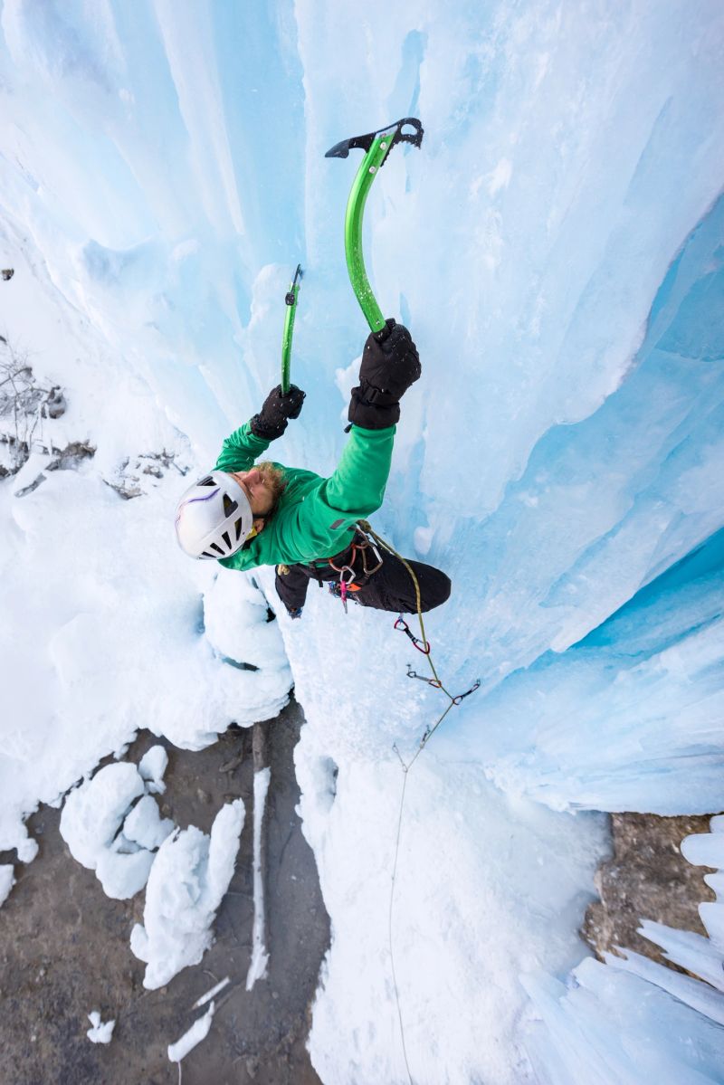 Determined male alpinist ice climbing on frozen waterfall on winter