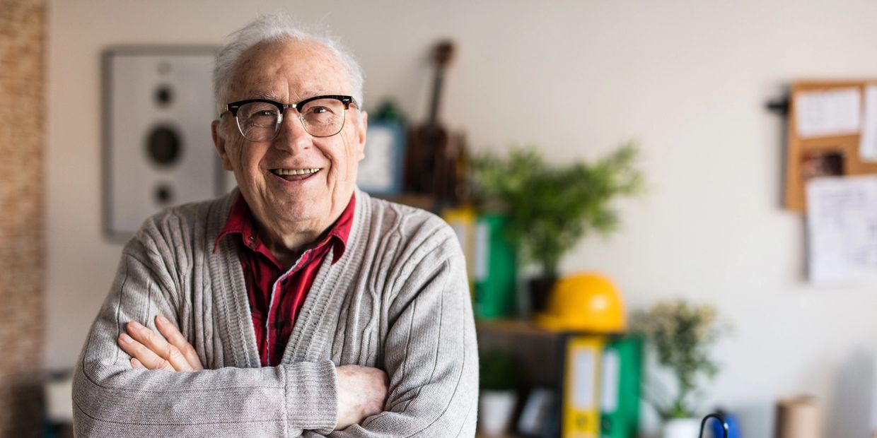 Smiling elderly man with glasses crossed arms indoors.